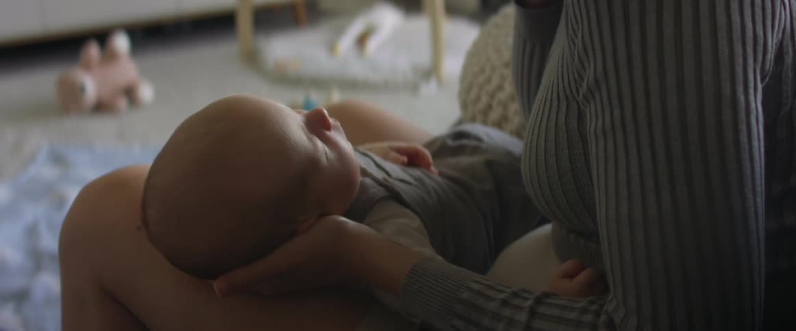 Mother holds her newborn asleep baby in her arms at home