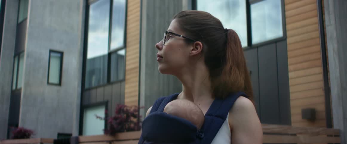 Mother standing near apartment building holds baby in a baby carrier