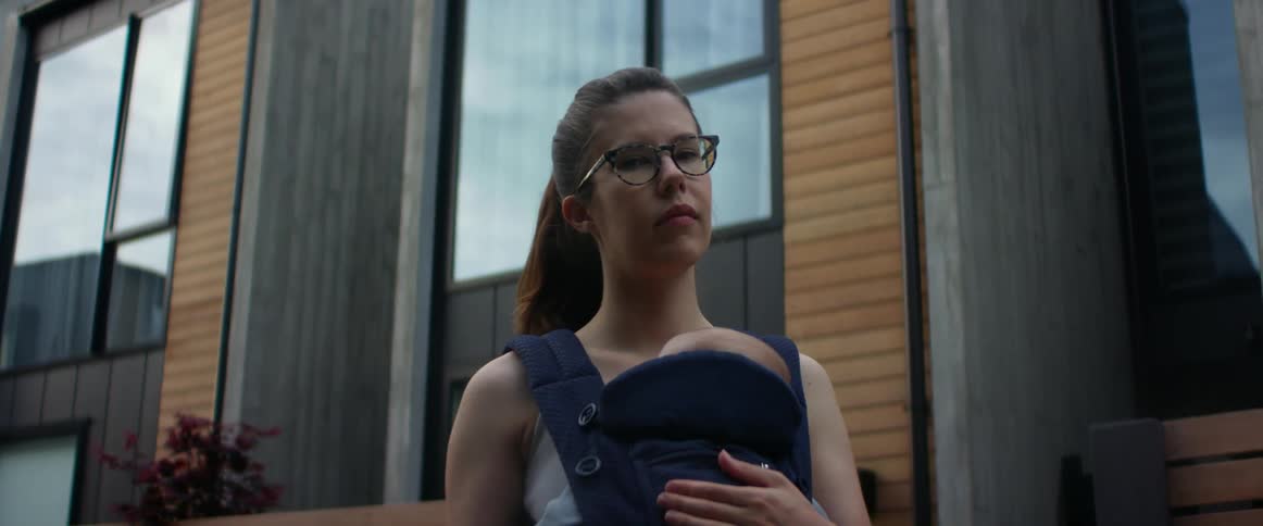 A mother holds her baby in a front carrier and stands looking off into the distance