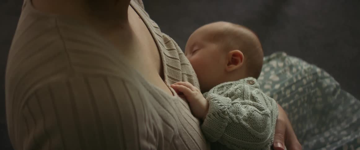 Mother sitting on couch and breastfeeding newborn infant child