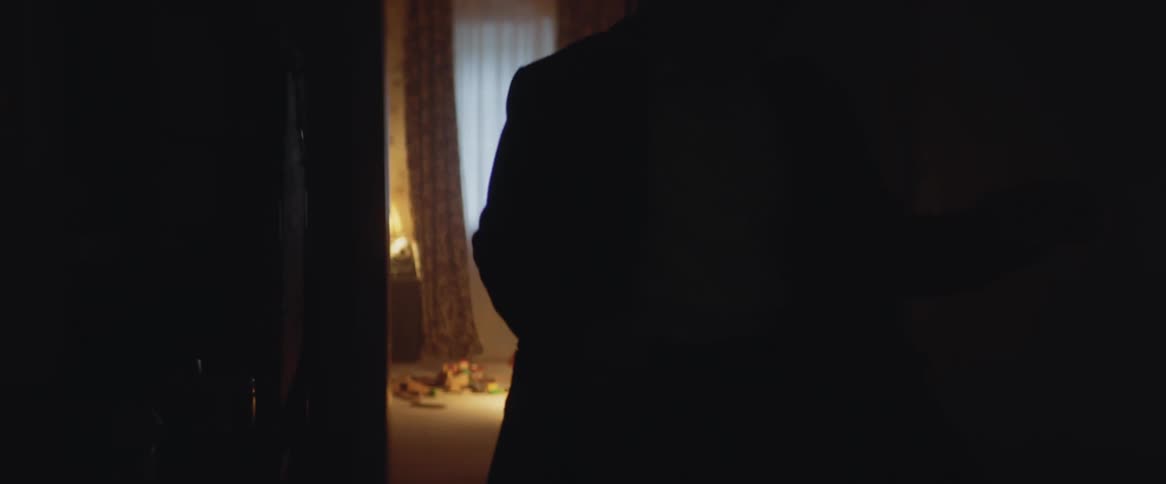 A man runs from a lit up room to a dark room where only his silhouette can be seen
