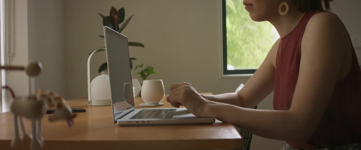 Woman with brown blouse and earrings types on laptop sitting at desk in room