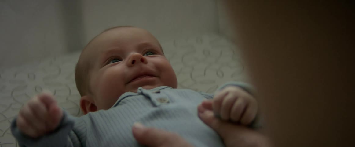 A newborn baby laying down in a crib with an adults hands on their belly