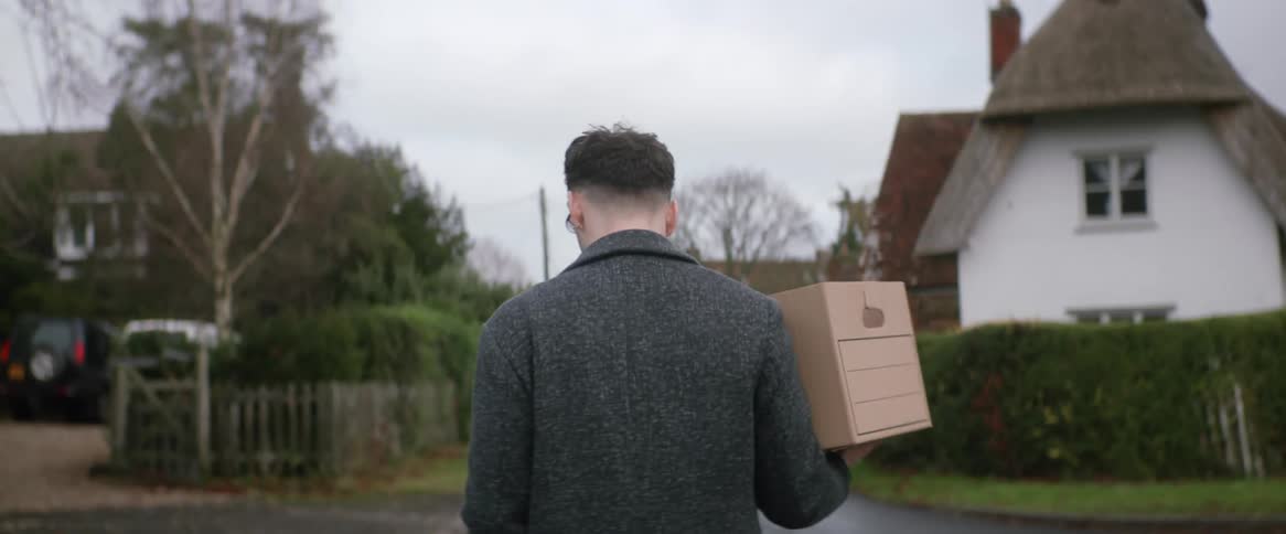 A man is carrying a box as he walks on a neighborhood street