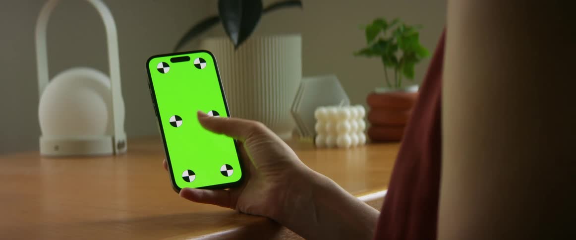 A woman is holding her cell phone and moving her thumb across a green screen