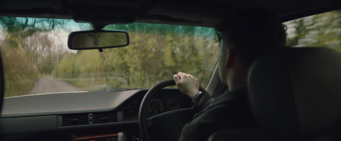 A man is driving an automobile on a country road lined with trees on a fall day