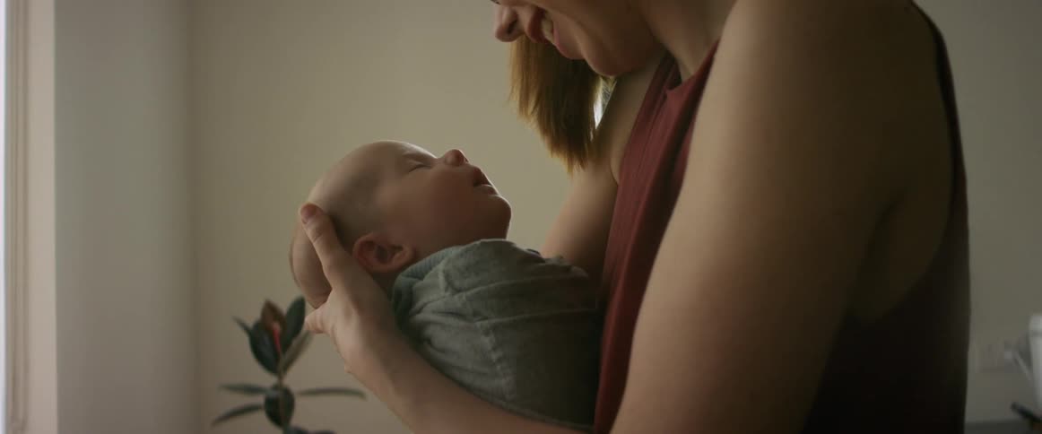 A mother holding her swaddled baby looking at it sentimentally