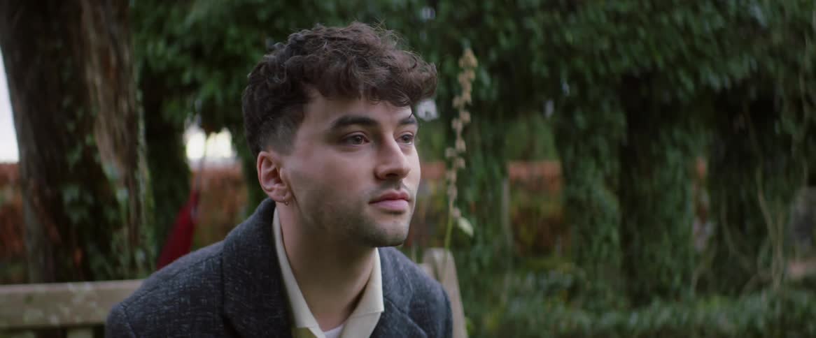 An up close of a mans face sitting on a bench outside
