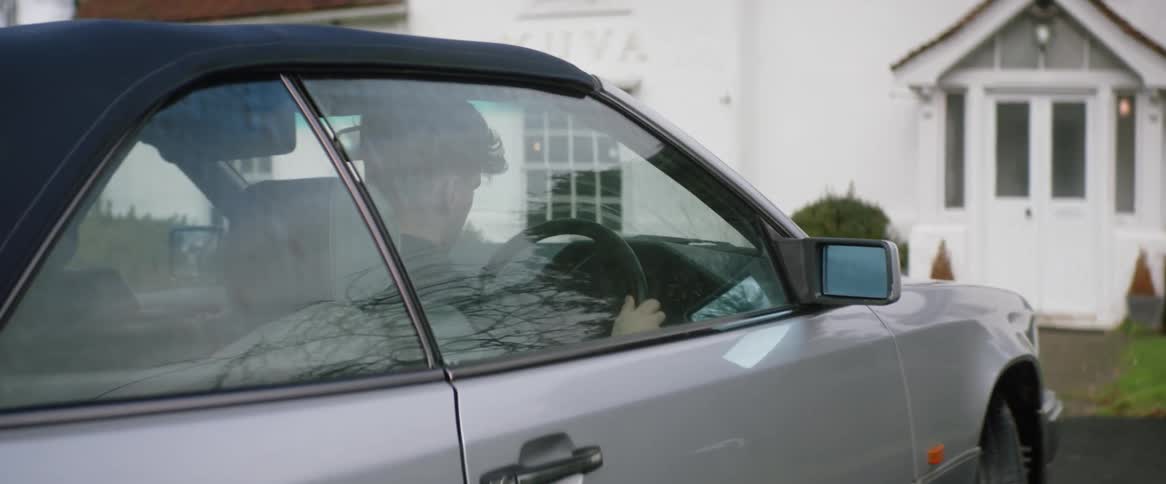 A man parking a car in front of a white house opening the car door and getting out