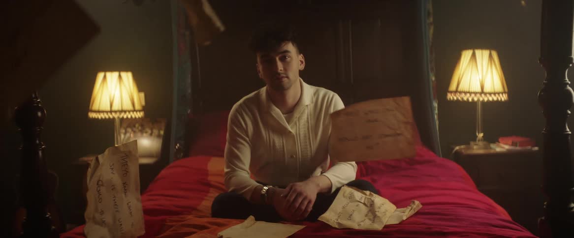 A man sits on a bed as papers fall down around him