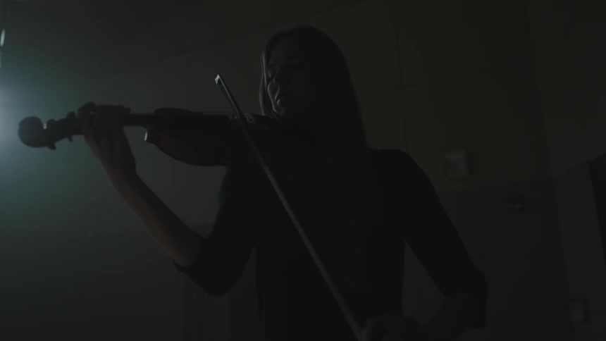 A violinist plays in a dim room