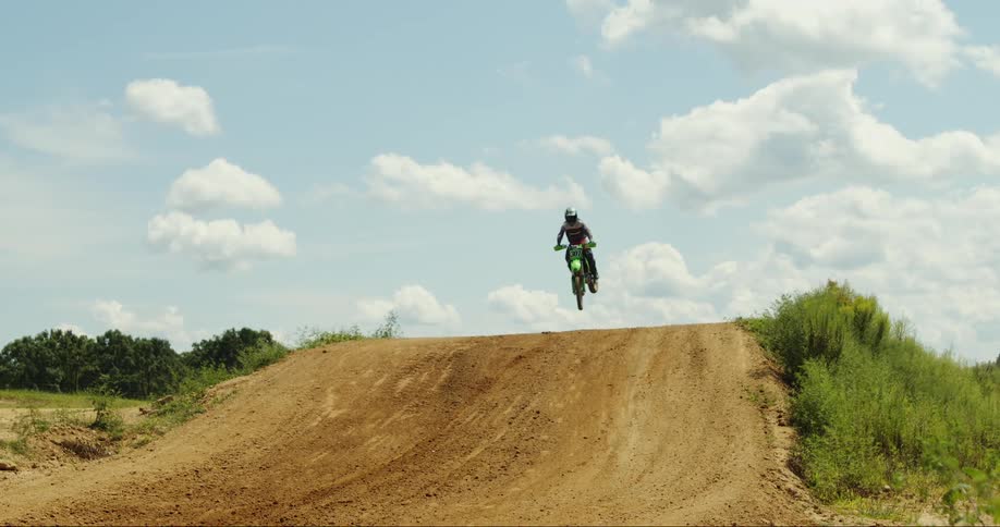 Motocross rider jumps over hill on course in countryside near pasture