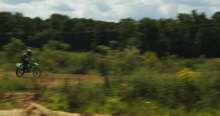 Motorcyclist rides motorcycle along road past woods and field