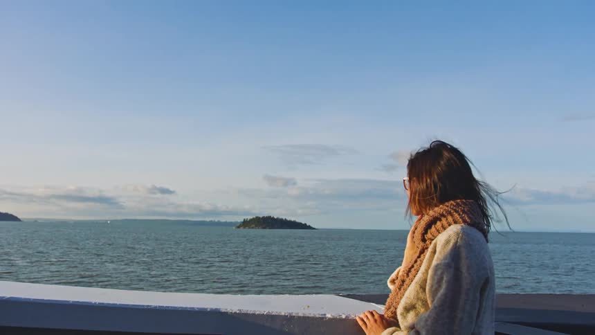 Young woman wearing a scarf looks at the ocean and islands from a boat at daytime