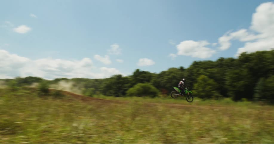 A person riding a dirt bike on a track and jumping it with trees in the background