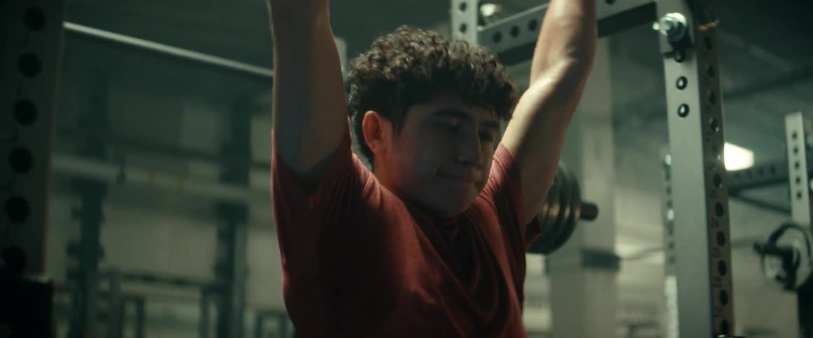 A teenage boy is working out in the gym holding a bar and pulling up his body and legs