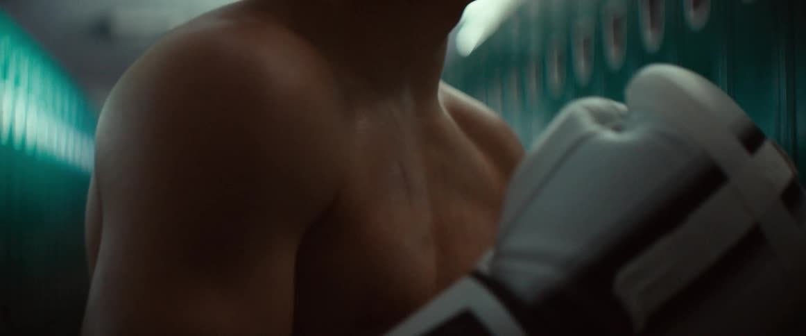Male boxer stands in locker room with gloves sweating