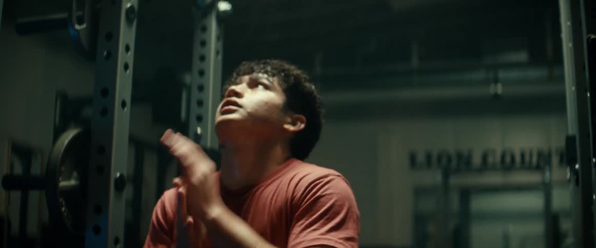 Man jumps up to pull up bar near weights in gym