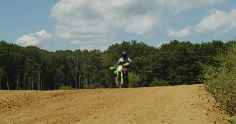 Motorcyclist jumps over hill on motocross course with forest in the background