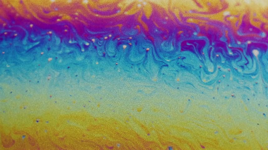 Fluorescent colors move and streaks blend as small particles float over the surface colors as they stretch