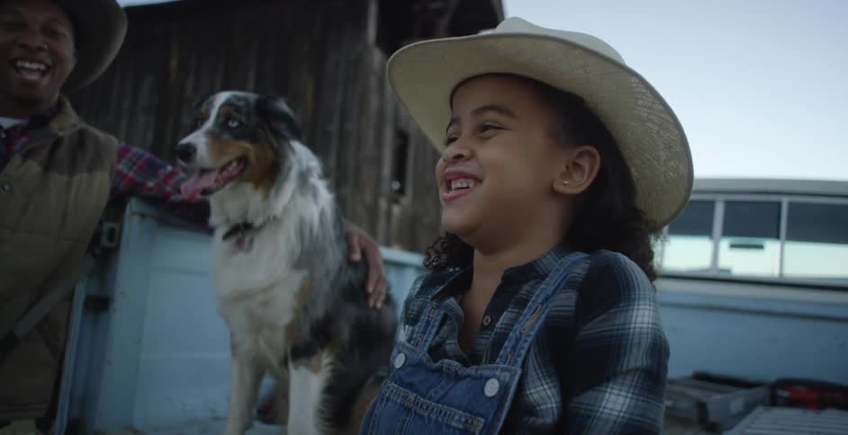 Father leans against pickup truck with hand on dogwatching daughter laugh