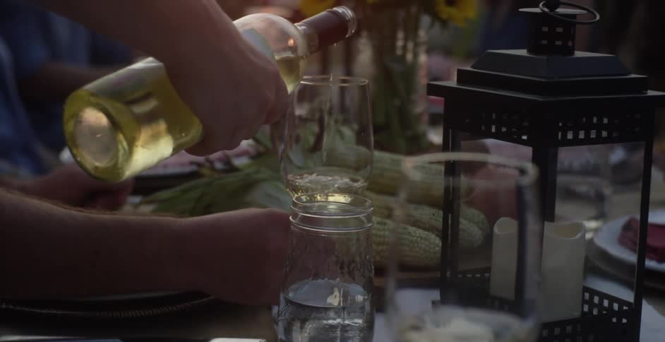 Man sitting at table at dinner party raises his wine glass in a toast after it is filled