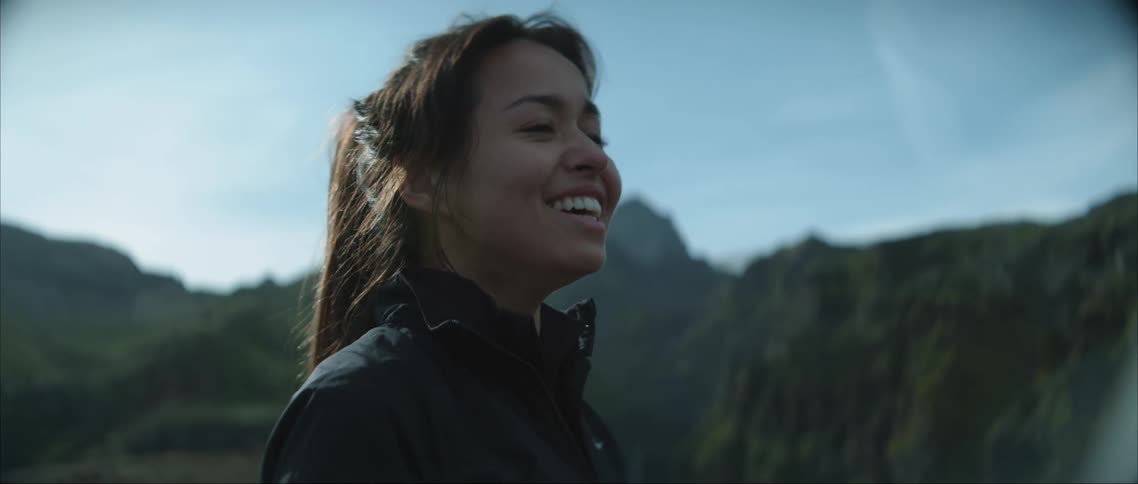 Young woman in nature surrounded by forested mountains laughing and crying of joy while watching someone off camera playing with soap bubbles
