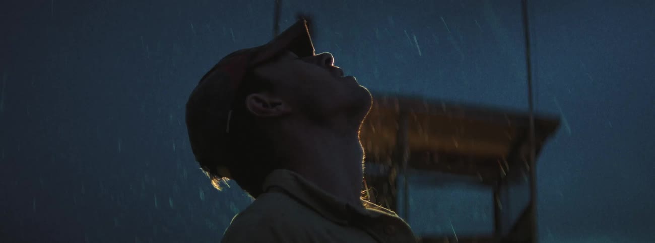 A man standing outside with his head uplifted during a rainstorm