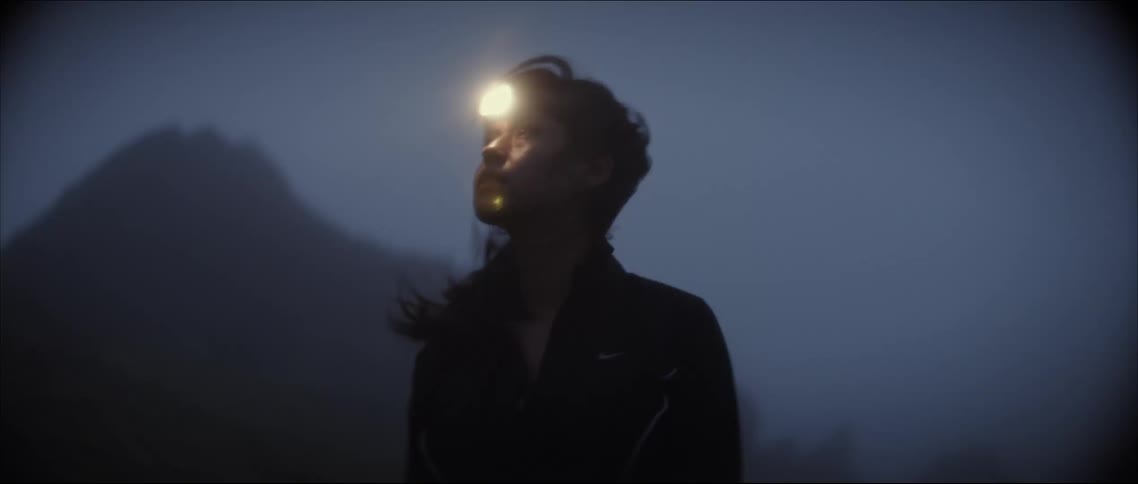 Woman wearing headlamp looks around foggy landscape near hill