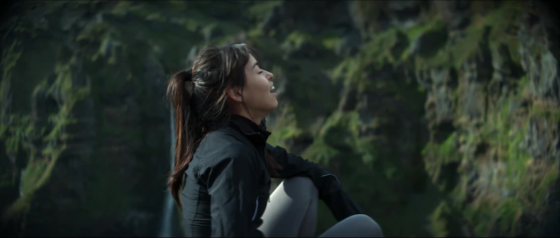Woman smiles as she sits down to rest across from waterfall and cliff