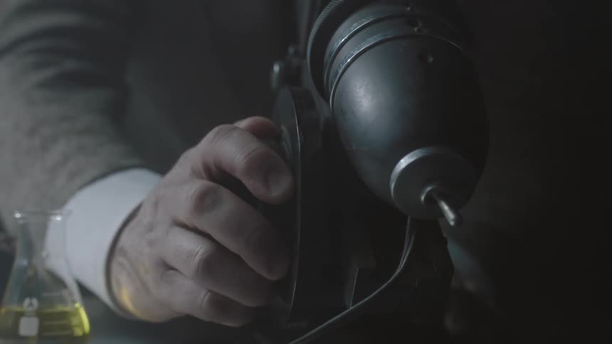 A hand adjusts a knob on a microscope