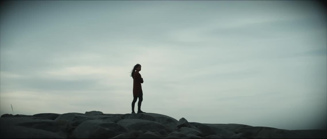 A silhouetted woman stopping to enjoy the view while walking on rocky ground in nature