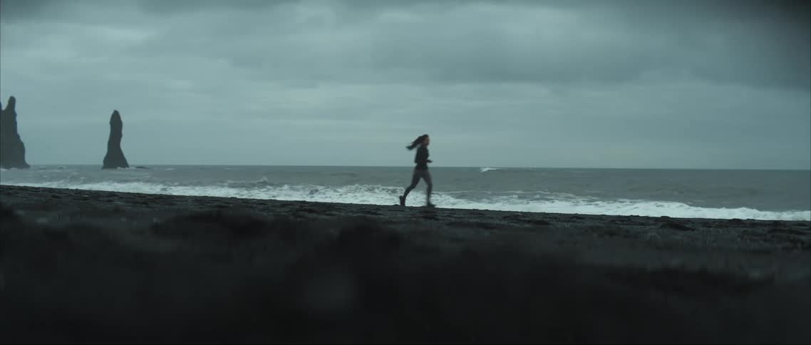 Woman exercising on a rocky beach at dusk on a cloudy day with the ocean in the background