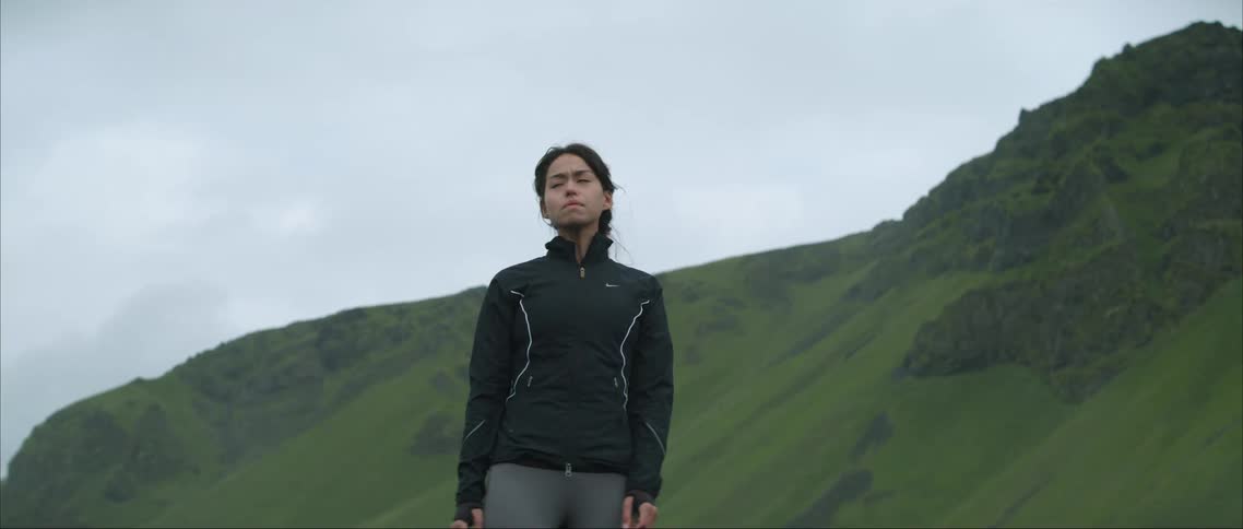 A woman stopped for a break while jogging in a hilly landscape