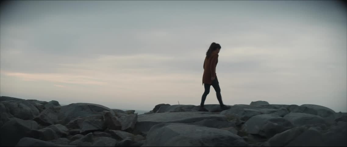 A silhouetted woman walking over rocky ground