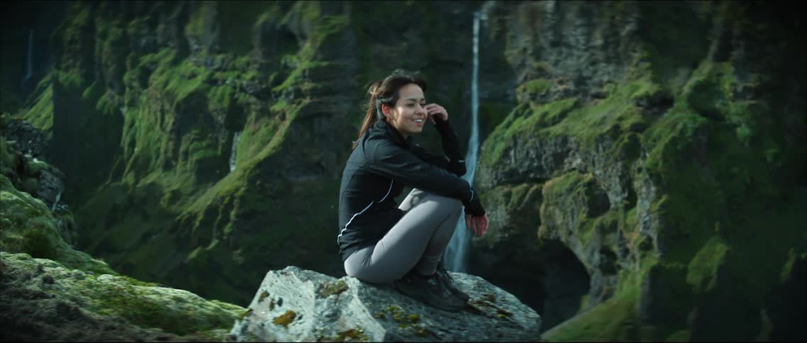 A woman sits on a rock by the waterfall