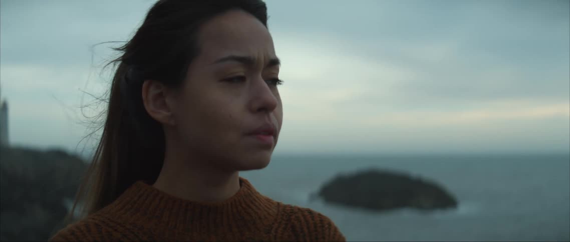 A close up of a womans face as she walks on a coastline looking sad