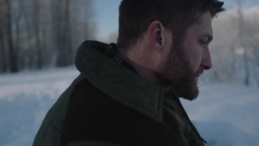 A man is standing in the snow as another is walking in the distance