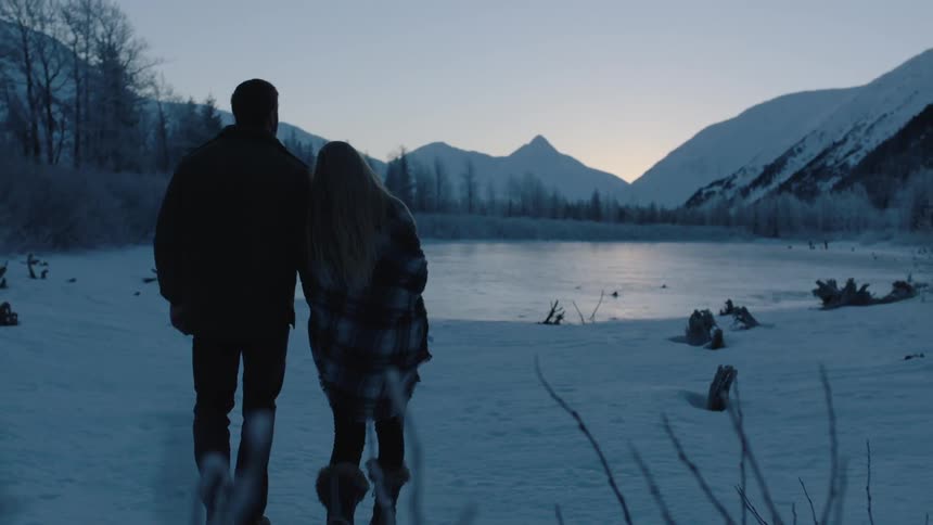 A man and woman walking through the snow toward a pond