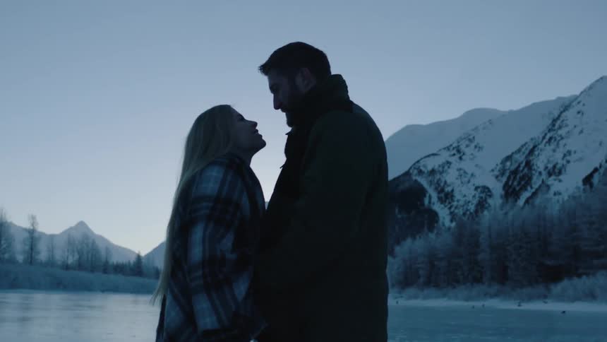A man and woman stand close together near a snow covered mountain