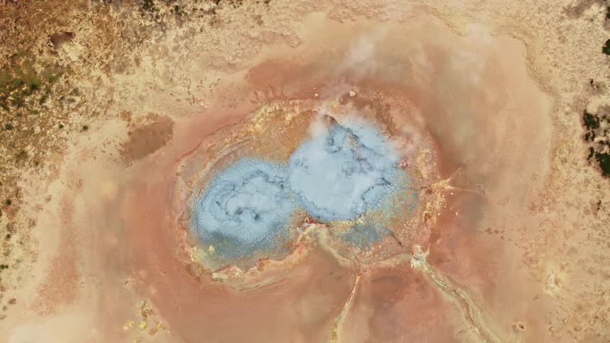 Smoke rises from a light blue bubbling area in the center of a terrain made of shades of gold and tan with darker texture further from the middle