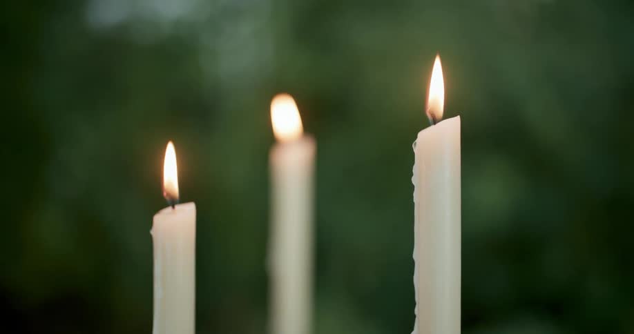 Three white candles are lit and the flames are wavering outside with trees in the distance