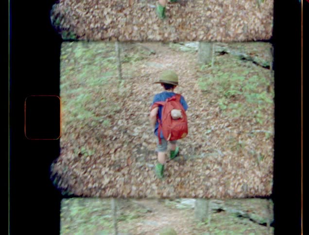 Young girl hikes through woods wearing red backpack holding teddy bear