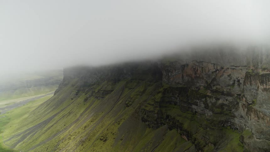 Fog settling over a mountain canyon and cliff with green grass growing down the side