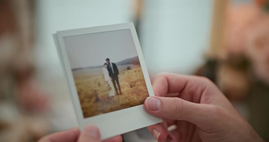 A person gestures with their hand while holding a photograph of a man and woman