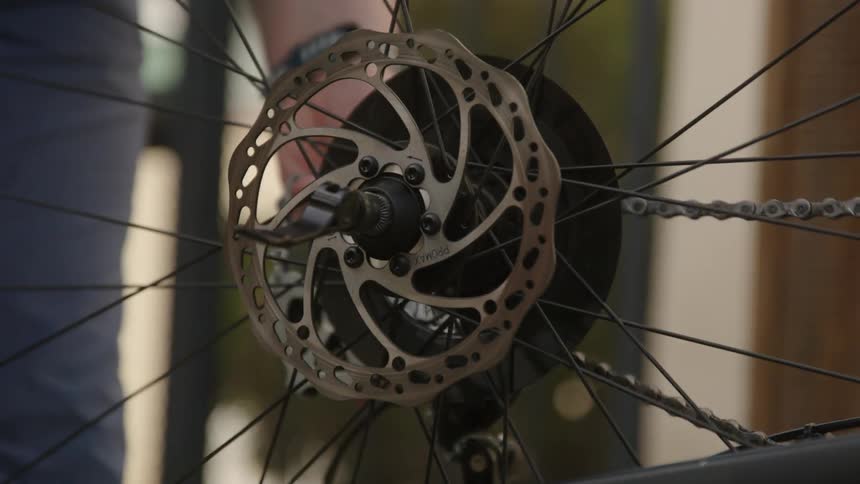 The chain of a bicycle is moving as a man puts the rear wheel on and moves the derailleur
