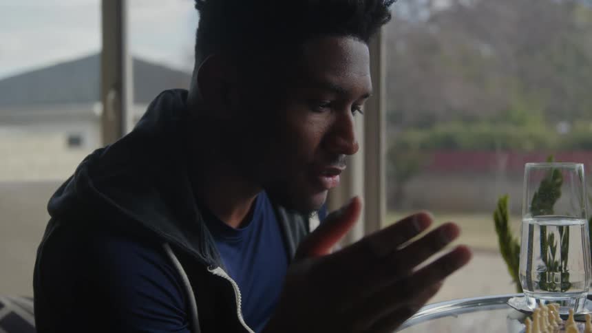 A close up of a mans face moving his hands sitting at a table