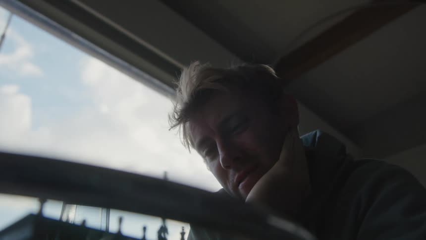 A man is sitting at a glass table playing chess near a window