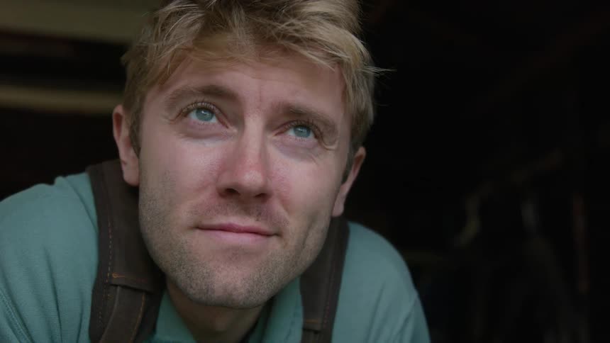 A man smiling while deep in thought with a breeze blowing through his hair