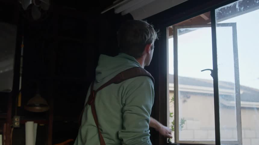 A man cleans his kitchen window with a rag before closing it